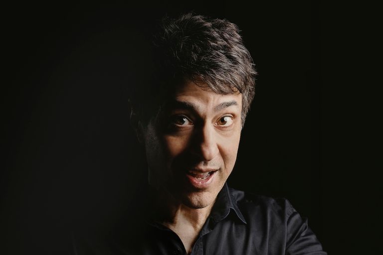 Portrait of stand-up comedian Arj Barker against a dark background.